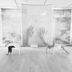 Two sets of legs visible behind large fabric panels with images of hands and clouds