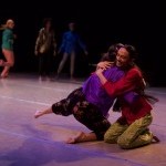 image of 2 performers embracing and smiling on the ground in bright, colorful clothing