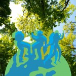 Image is of silhouetted dancers dancing on an icon of the earth with blue sky and trees behind them.