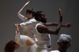 Dancers dressed in white face away from one another, holding one arm at a ninety-degree angle and the other flat.