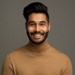 An artist from India, wearing a turtleneck and smiling because he’s happy pursuing his dream in NYC