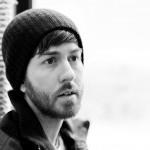 A black and white picture of Jason looking away from the camera lens; he is wearing a black beanie and has a shorter beard.
