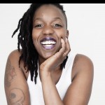 Smiling Black woman wearing a white tank top in front of a white background