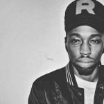 Black nd white image of a Black Man wearing a baseball cap with the letter R on it and a dark jacket with white t shirt.