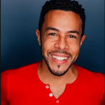 Smiling man with dark hair in a red shirt in front of a blue background