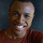 Smiling man wearing a red shirt in front of a dark background