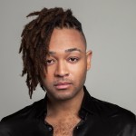 Jeremy is a Black man with shoulder length dreadlocks swopped to one side of his confidently focused facial expression.