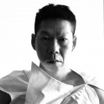 Black and white photo of a man in a black t shirt in front of a white background