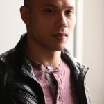 Mixed race man half Asian half Eastern European man in his 30s with medium length black/brown hair. Wearing a leather jacket