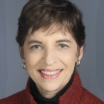 White woman with short brown hair, red jacket, gold earrings