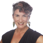White queer femme with multicolored short hair, smiling at the camera, wearing a red lip with a velvet top with a lace design.
