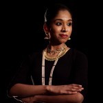 South Asian woman with arms crossed, wearing a dark shirt and looking off to the side