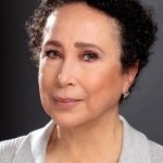 Virginia is a light-complexioned Black woman with dark, short curly hair wearing a light gray v-neck sweater. 