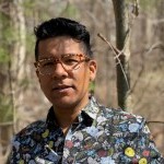 Headshot of Dr. Luis wearing a floral patterned button down in the woods.