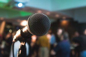 An image of a microphone in front of a blurred out crowded auditorium