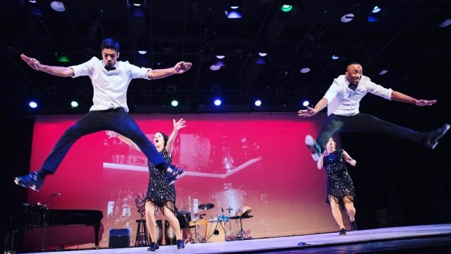 Tap dancers leap enthusiastically in a straddle position on stage
