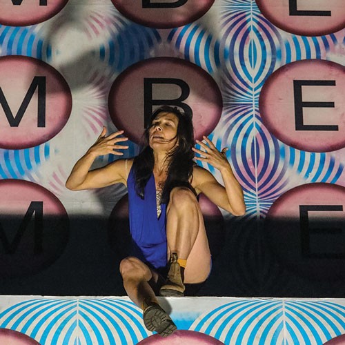 a woman sits on a ledge breathing in with hands by her side in a blue outfit