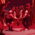 Two people come together in red lighting with hands outstretched