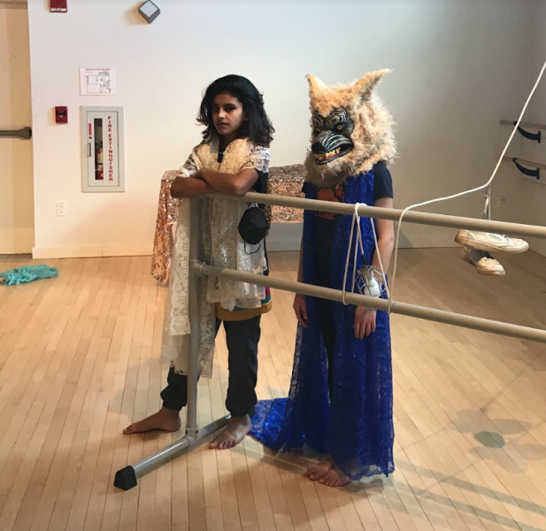 two children stand behind a ballet barre, one with a wolf mask on in blue lace and the other with long hair gazing at the camera