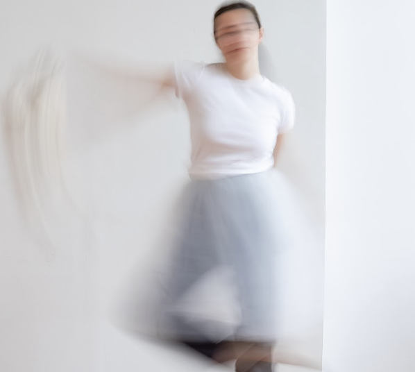 a white femme dancer with white shirt and light blue pants lifts her knee and arm in a blurred motion image