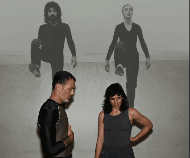 Molly and Wally stand in front of a projected black and white image of David + Valda.