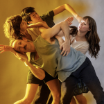 four dancers create angular shapes, their bodies intertwine, a soft yellow light fills the left side of the image 