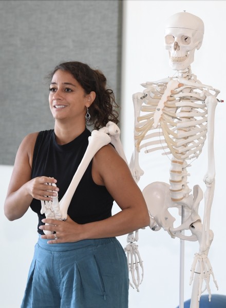 The photo shows Allegra with a skeleton model behind her. She has the right leg of the skeleton over her shoulder. 