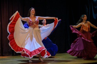 Three Reaction Dance company members dance on a stage with a black backdrop and wood floor.
