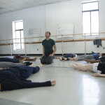 seated dancer, gazing upwards, surrounded by dancers lying on their backs