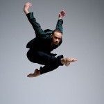 White background with a male dancer in a green long sleeve shirt and black pants
