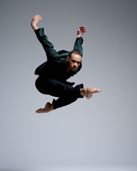 White background with a male dancer in a green long sleeve shirt and black pants