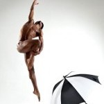White background with a African-American man doing ballet with a black and white umbrella on the floor