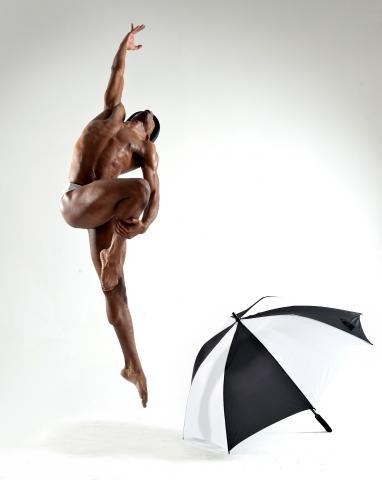 White background with a African-American man doing ballet with a black and white umbrella on the floor