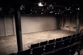 Image of a theatre stage with bright lighting and audience seats facing the stage
