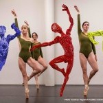 Dancers are posed with steel statues in bright vibrant primary colors. 