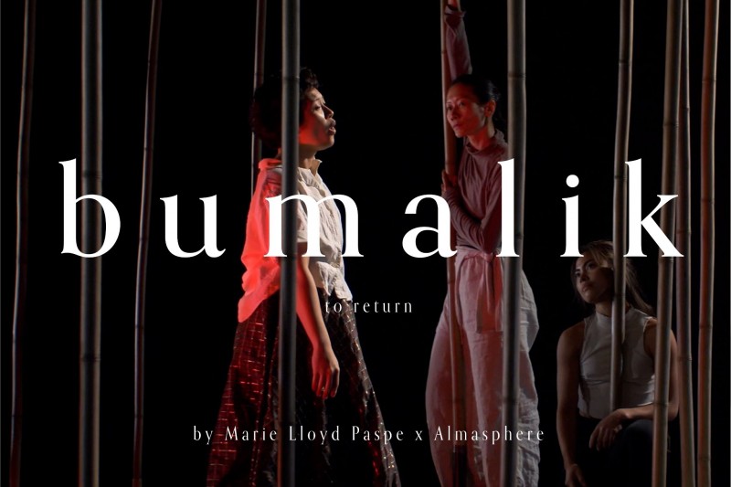 two dancers leaning on tall bamboo sculptures, watching a third dancer in Filipino-inspired attire, move through the bamboo