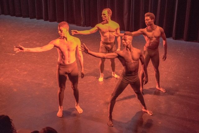 Four topless dancers extending their arms in one direction.