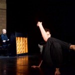 Image of a dancer sitting with legs crossed an one hand bent at the elbow 