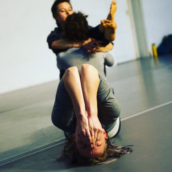 Image of a dancer with her head on the floor, chin up with bands covering her mouth
