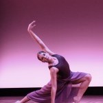 A dancer is wearing a flowing purple skirt in a lunge one arm up with other hand touching the floor