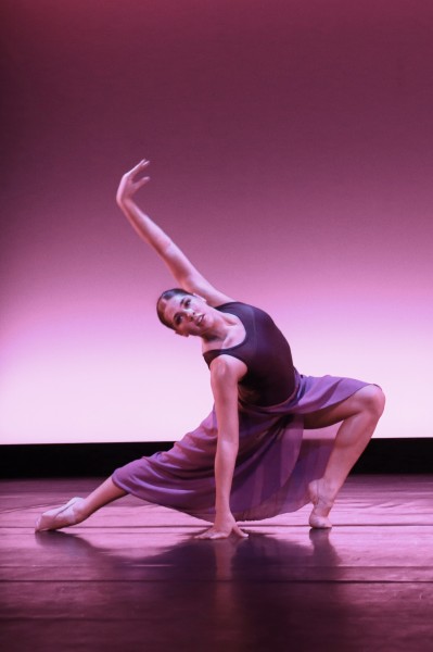 A dancer is wearing a flowing purple skirt in a lunge one arm up with other hand touching the floor