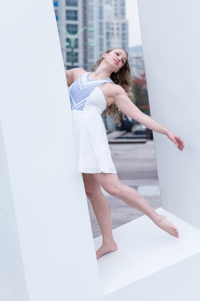 The choreographer on a white sculpture, leaning back with her left arm extended toward the earth.