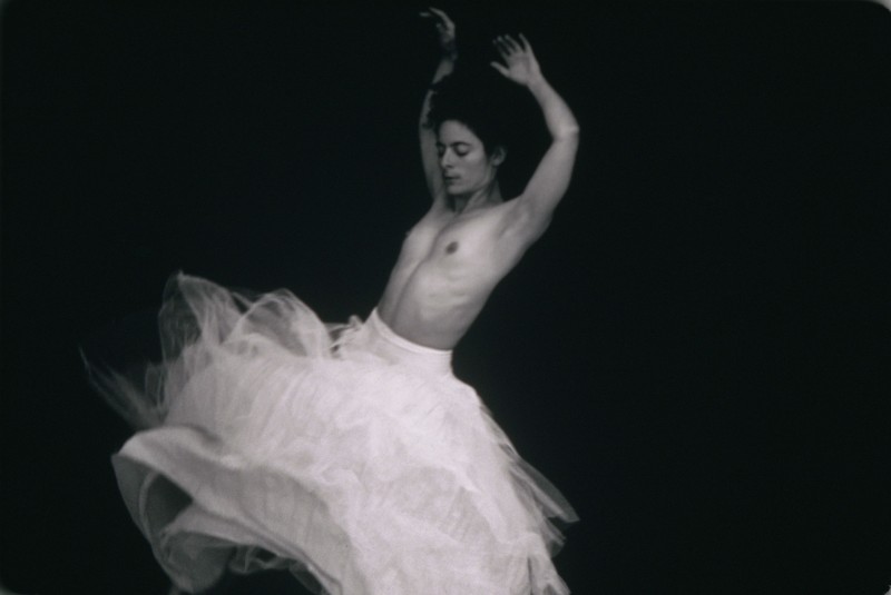 Black and white image of a woman swirling around topless in a flowy white skirt