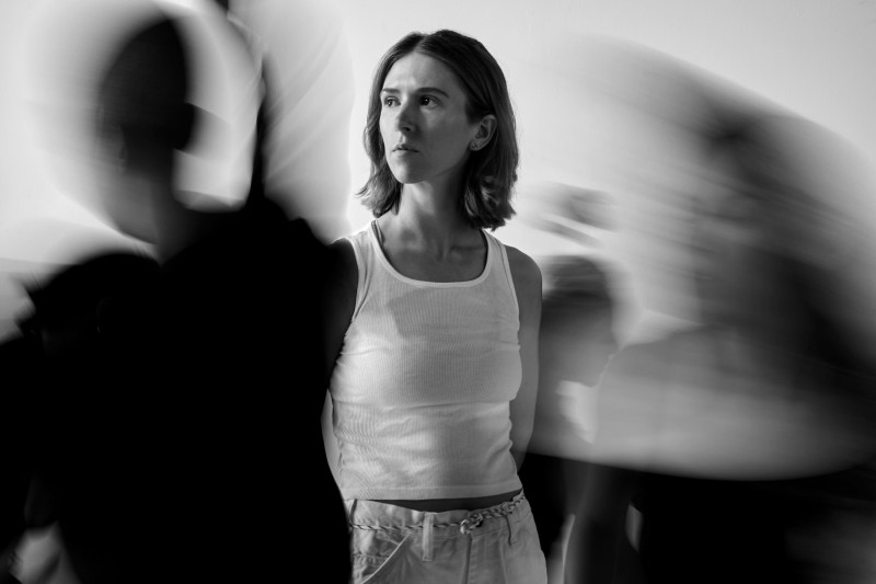 A person stands still in the middle of whirling bodies in motion that surround them and create a feeling of chaos.