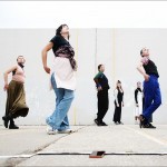 dancers in casual clothes look upwards, one leg crossed over the other