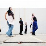 dancers in casual clothes look upwards, one leg crossed over the other