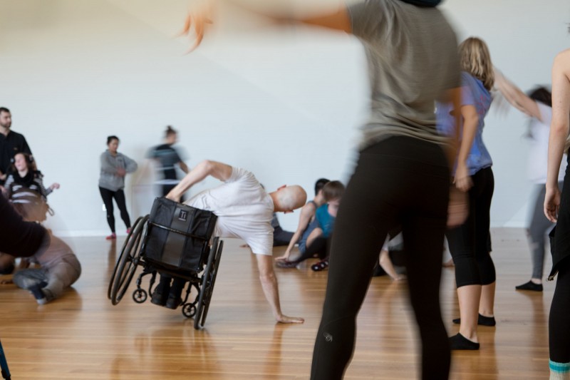 A dancer on the left tilting his wheelchair and a dancer on the right standing with arm outstretched. 