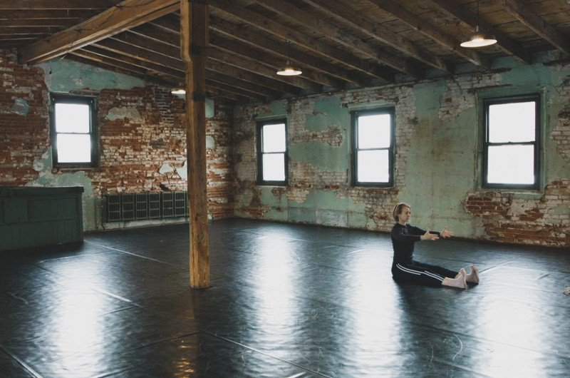 Dancer stretching in The Iron Factory dance studio - marley flooring, exposed brick walls, wooden beams