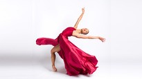 Single dancer in red dress in standing fourth position cambre back.