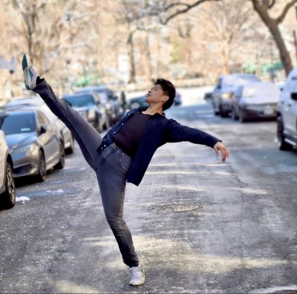 Full-body action shot of a male dancer in a dynamic pose on a New York City street, showcasing urban style